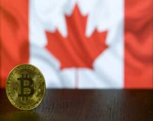 Gold Bitcoin coin on a wooden surface with a Canadian flag blurred in the background
