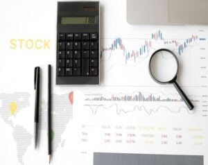 Calculator, magnifying glass, and financial charts on a stock analysis desk.