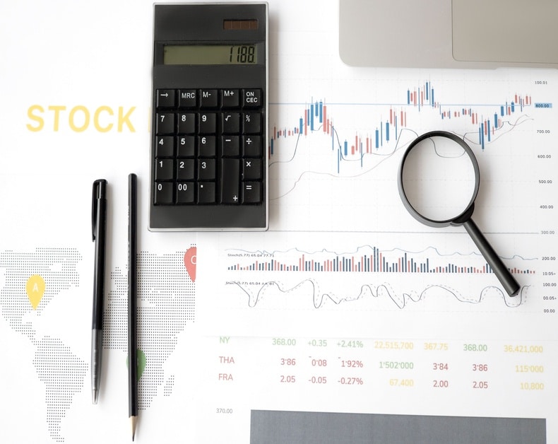 Calculator, magnifying glass, and financial charts on a stock analysis desk.