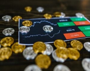 Close-up of a crypto trading screen with a fluctuating chart, surrounded by gold and silver coins on a wooden table.