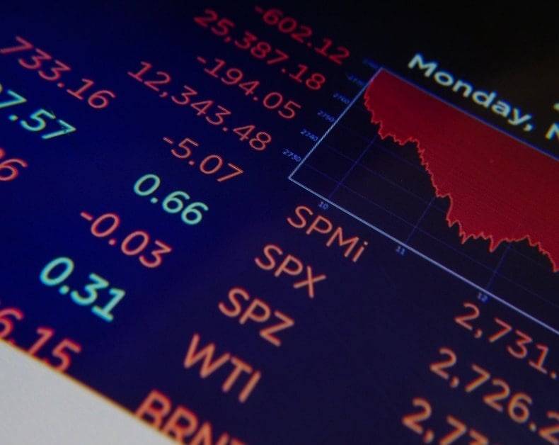 Stock market dashboard showing a red downward-trending chart and fluctuating numbers on a dark screen.