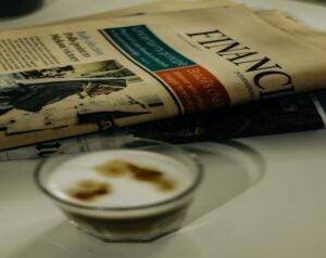 Folded newspaper with bold headlines lying on a table, a glass of coffee in the foreground.