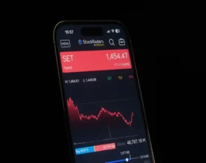 Smartphone screen showing stock trading app with SET index at 1,454.47 in a red banner and a stock chart nearby.