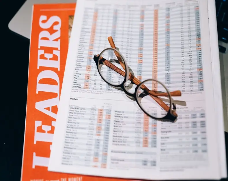 Glasses resting on a financial report with charts and numbers atop an orange LEADERS magazine